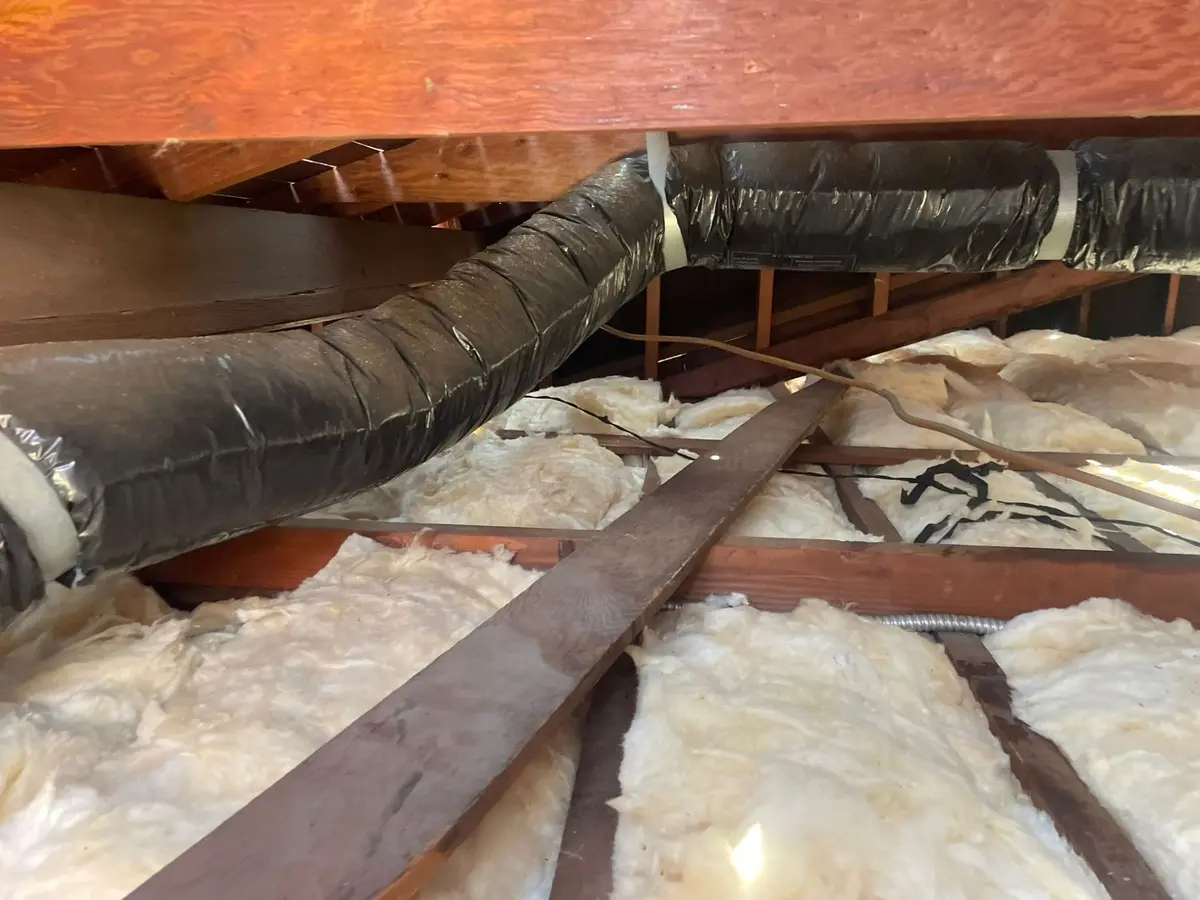 Fiberglass batt insulation between attic floor joists with insulated flex ductwork running overhead